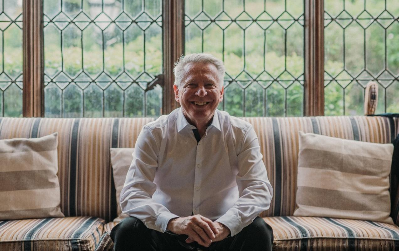 Nick smiling, sitting on a sofa in front of a leaded window