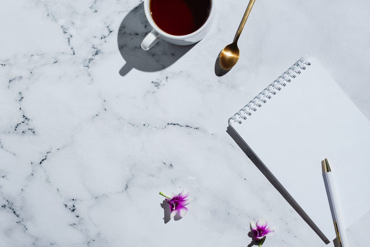 A cup of tea beside an open notebook and pen