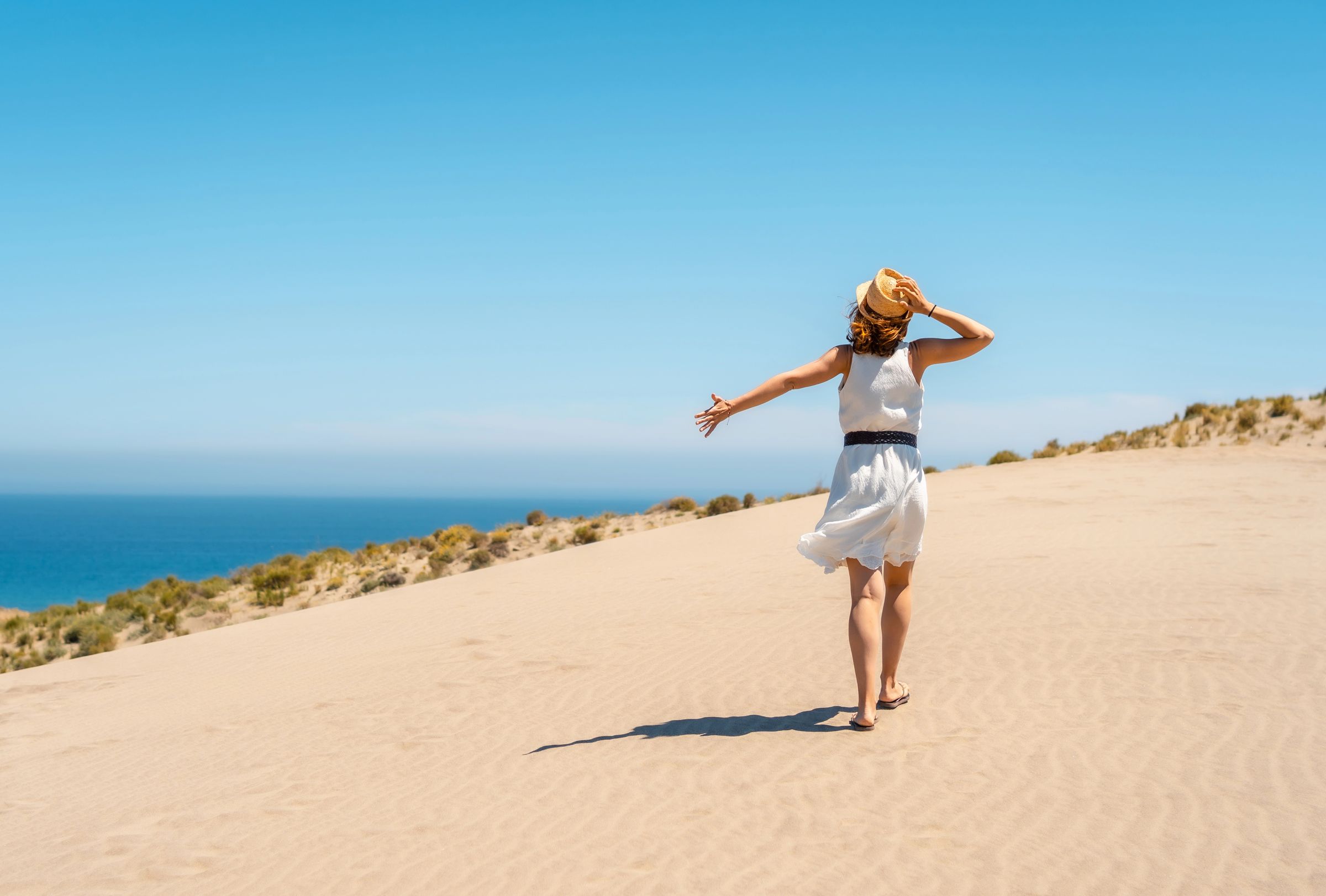 A woman walking freely along a coastal path toward the sea, arms open